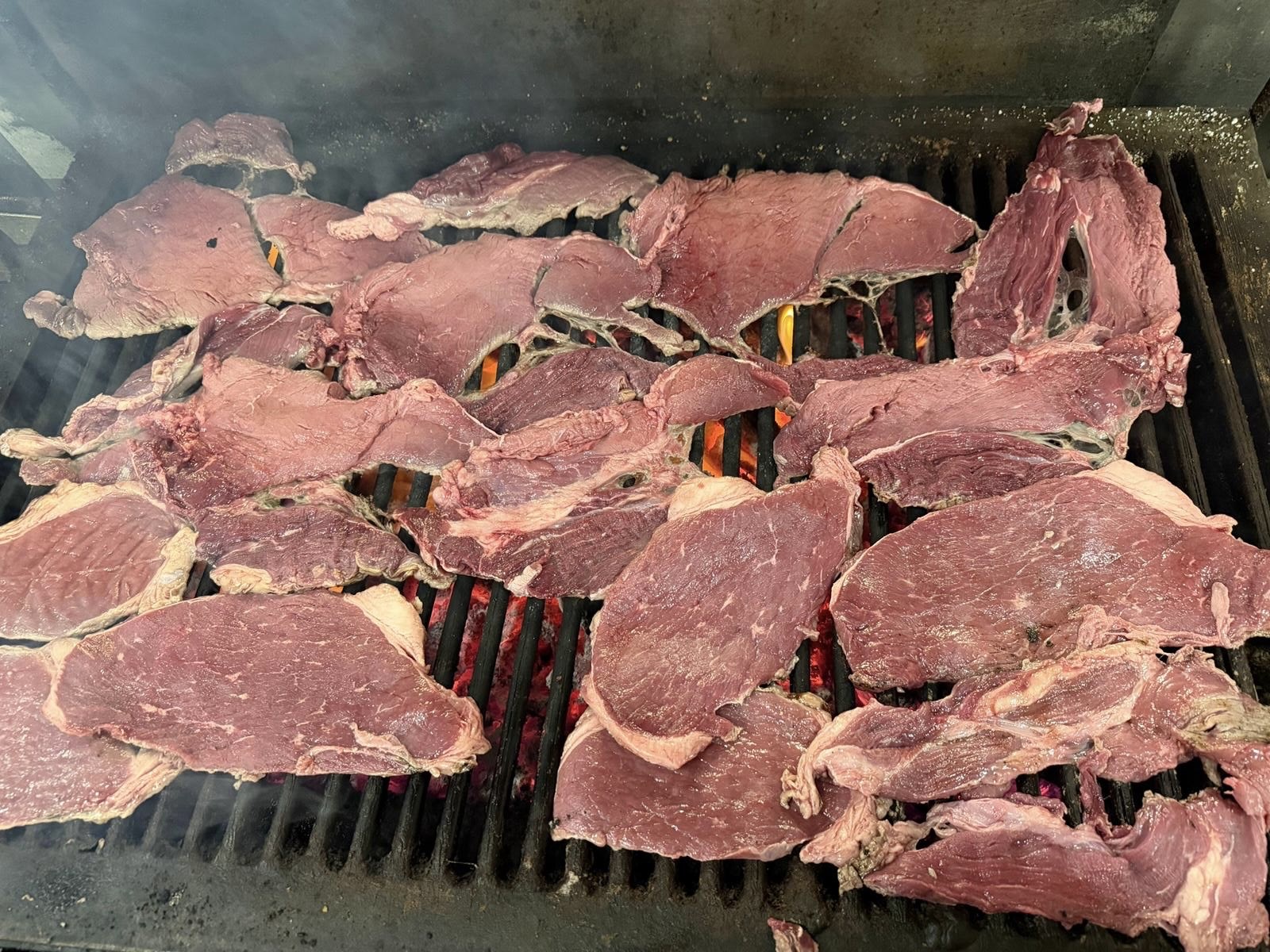 Carne asada grilling over an open mesquite flame for catering